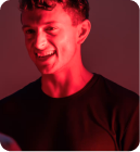 Vital Red LIght. Red Light Therapy. A man wearing a dark t-shirt smiles under red lighting, featured as the main subject with a blurred background.